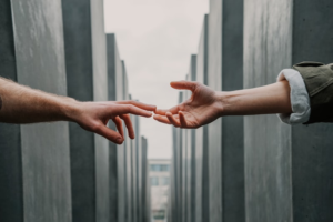 Alt Text:
Two hands reaching toward each other against a backdrop of concrete pillars, almost touching